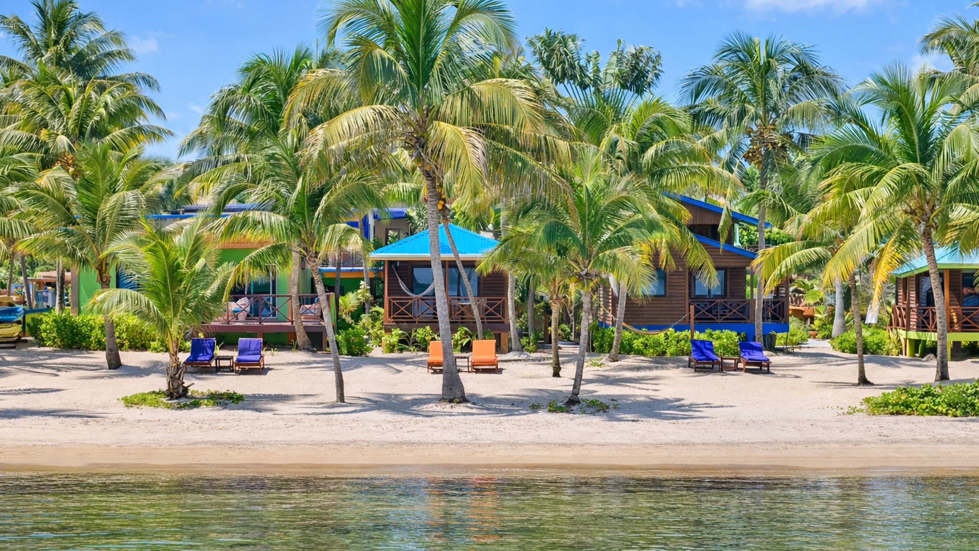 Tropical beach with palm trees and colorful cottages by the water.