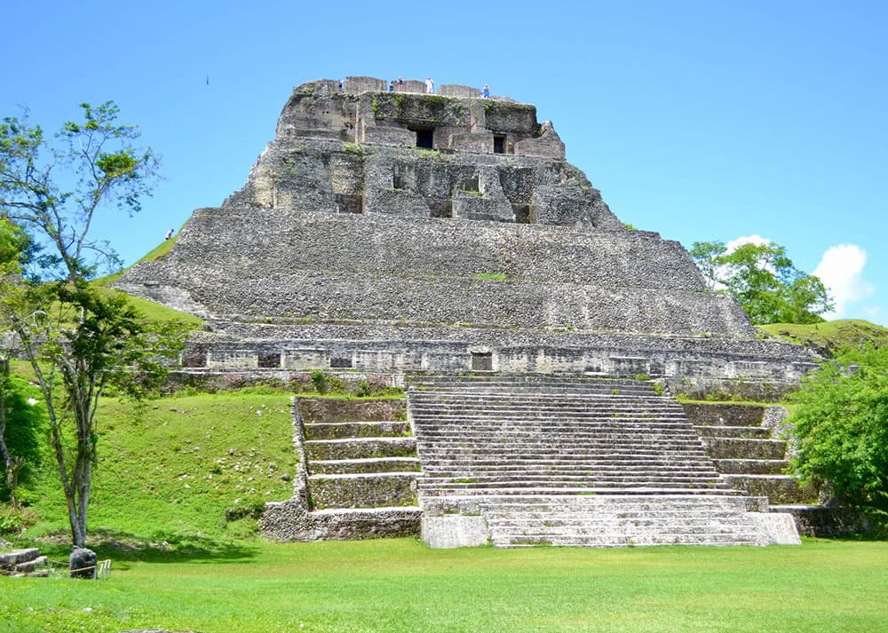 A large ancient pyramid with steep steps set against a clear blue sky and lush greenery.