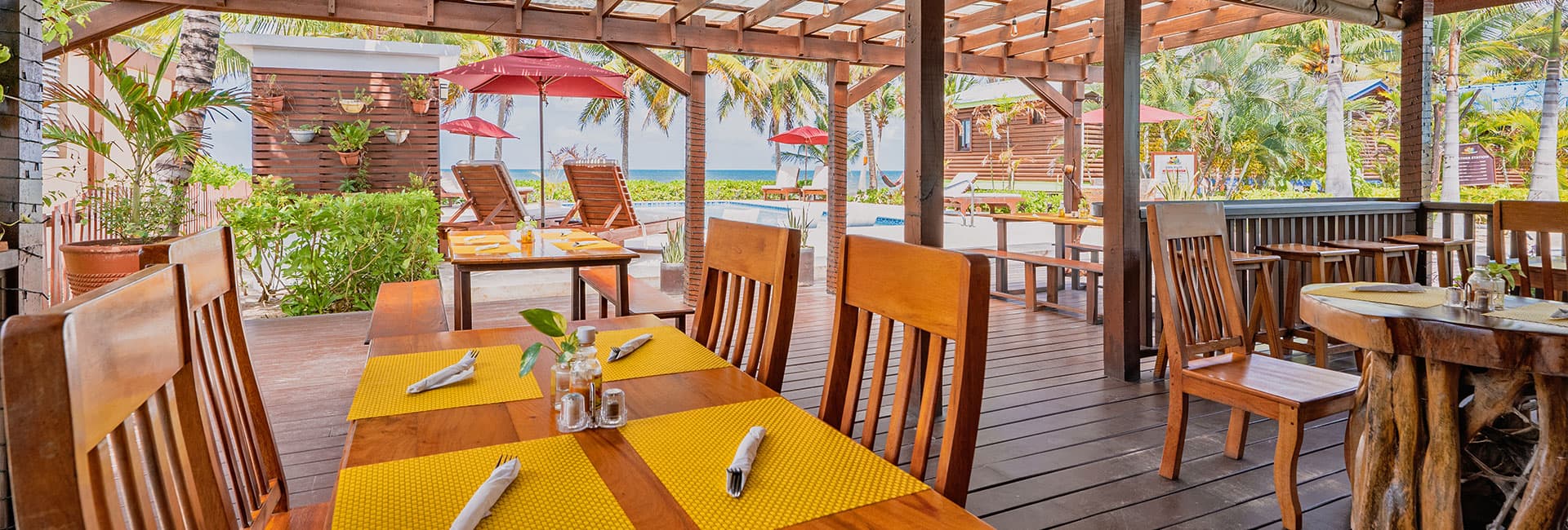 Outdoor dining area with wooden tables and chairs, overlooking a pool and tropical surroundings.