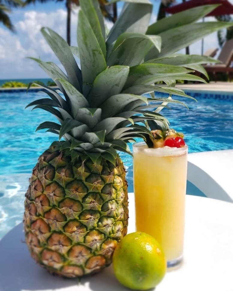 A pineapple and a lime next to a tropical cocktail by a pool.