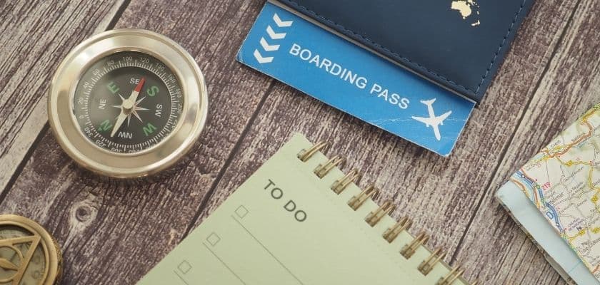 A compass, boarding pass, notepad, and map arranged on a wooden surface.