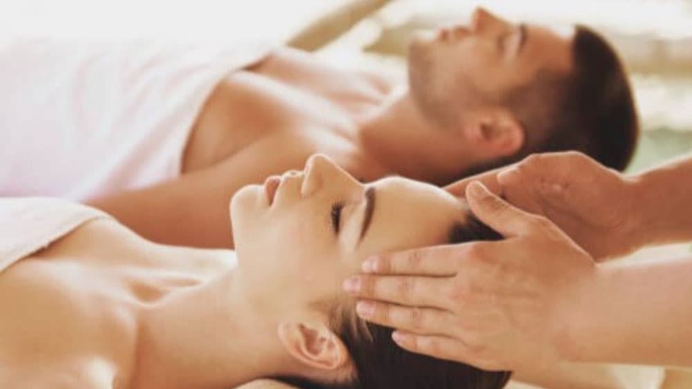 A woman receives a facial massage while a man relaxes nearby.