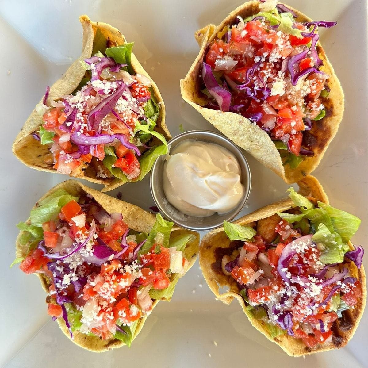 A plate of mini taco bowls filled with colorful vegetables and served with a side of creamy dip.