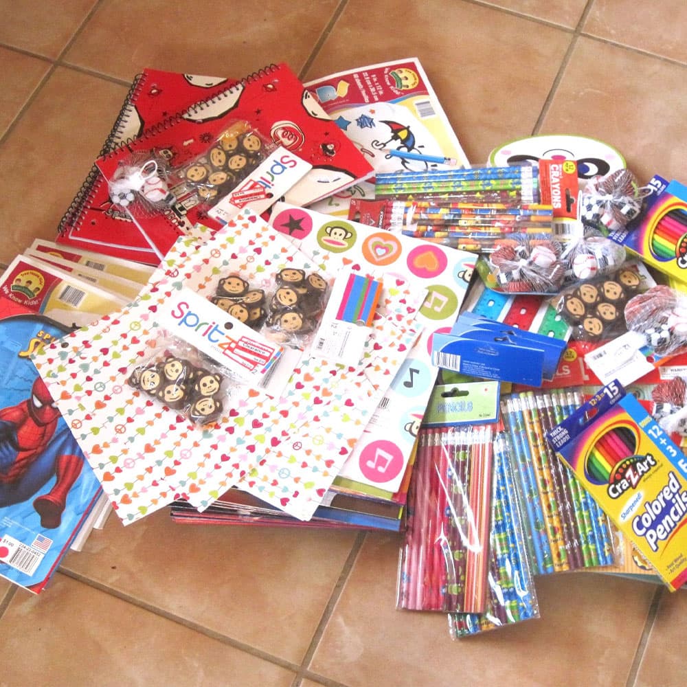 A colorful assortment of school supplies, including notebooks, pencils, stickers, and themed decorations, scattered on a tiled floor.