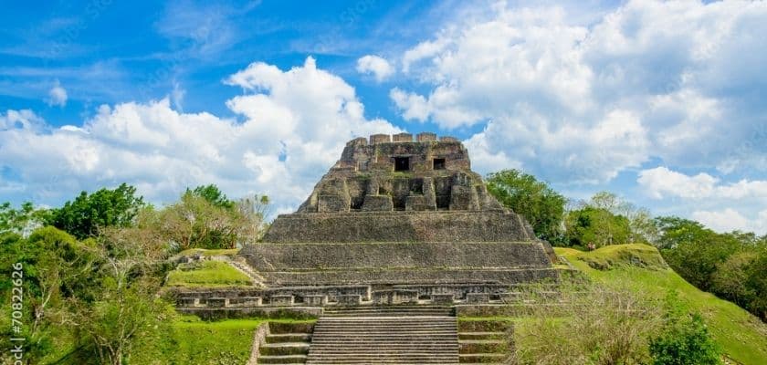 Ancient Maya ruins rise above green jungle under a bright blue sky in Belize.